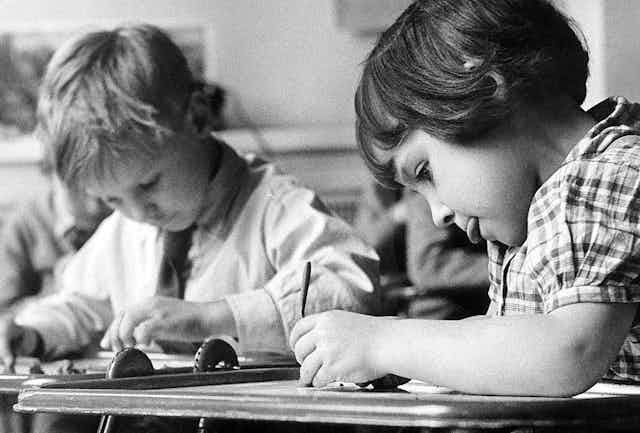 Black and white image of schoolchildren working at desks.