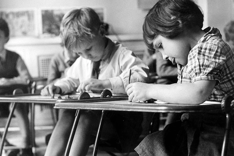 Black and white image of schoolchildren working at desks.