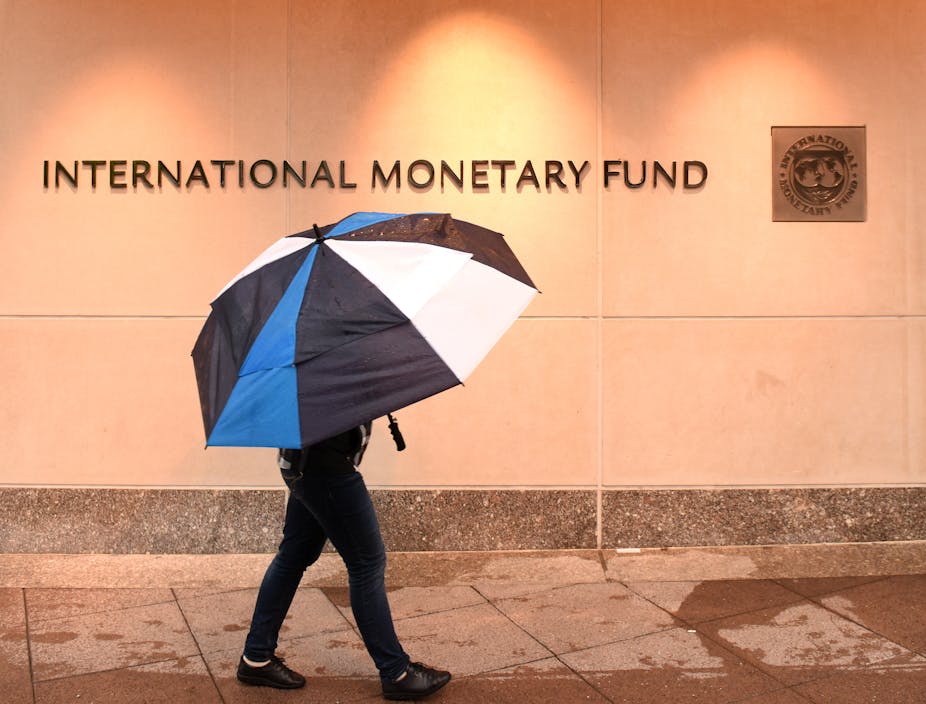 Person with umbrella walking past sign for International Monetary Fund