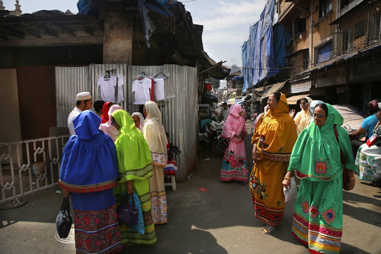 A group of women wearing colourful islamic dress walk along a street.