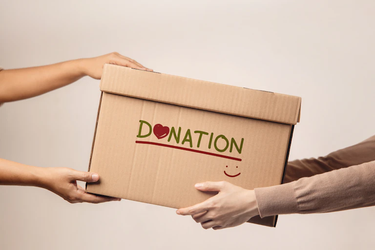 One pair of hands passing a box labelled 'donation' with a heart and happy face to another pair of Hans