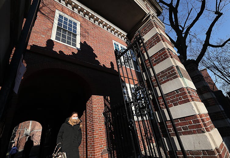 A person walks through brick gates, with a large brick building in the background.