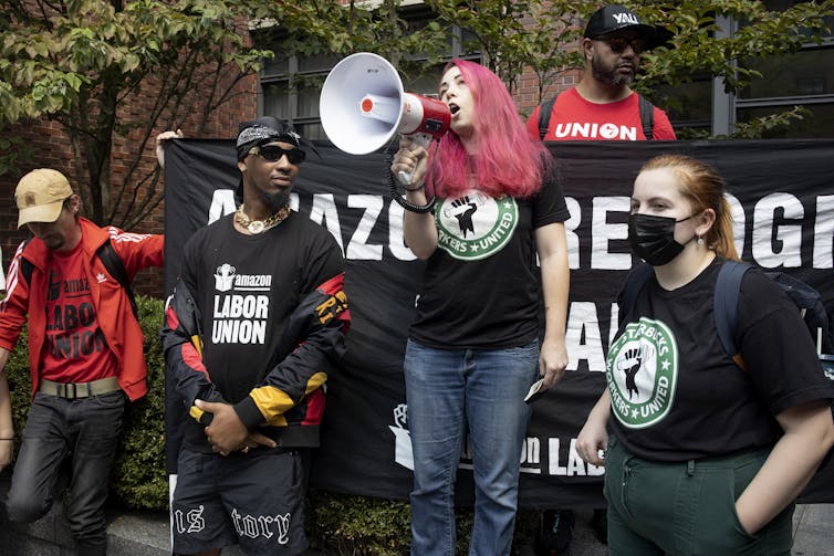 A woman with pink hair speaks into a megaphone surrounded by other union organizers wearing black