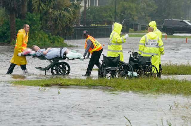 Emergency staff wheel a woman on a stretcher out of a nursing home through flood water up to the shins.