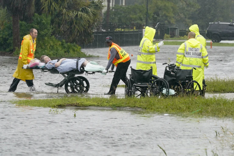 Emergency staff wheel a woman on a stretcher out of a nursing home through flood water up to the shins.