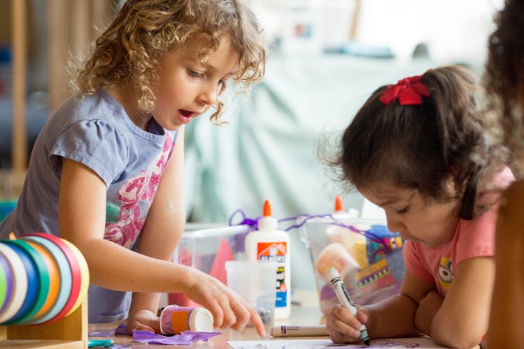 Children seen playing at a desk.