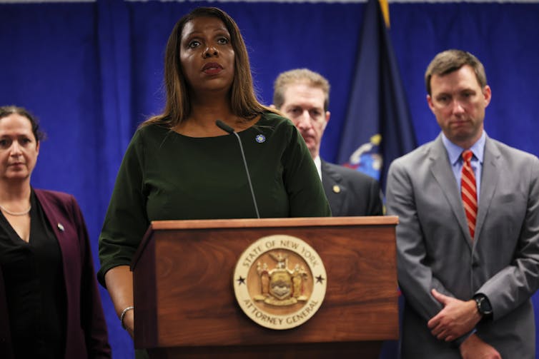 A Black woman in a green top stands behind a lectern.