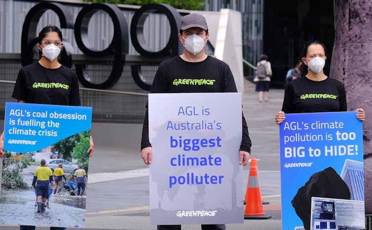 Three protesters in masks with signs against AGL