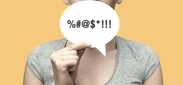 A woman holds a speech bubble with symbols in front of her mouth. 