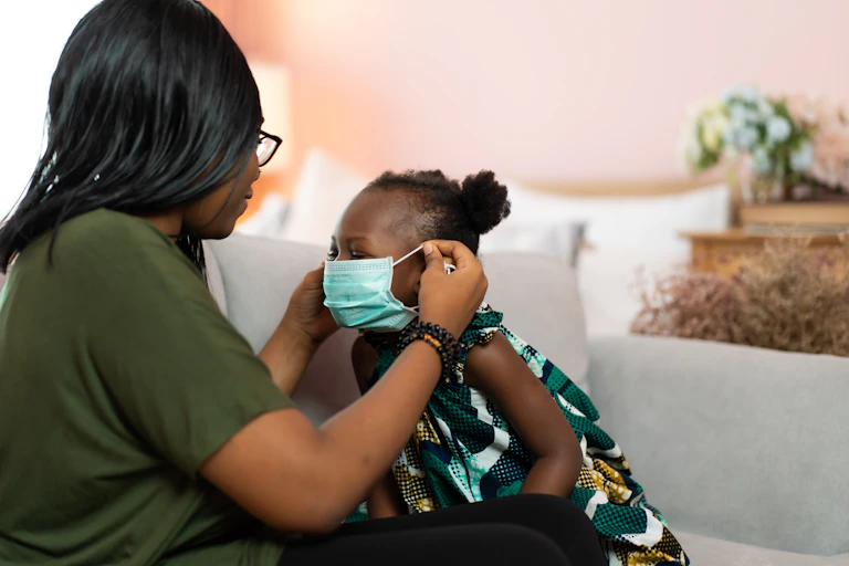 A parent puts a surgical face mask on their child.