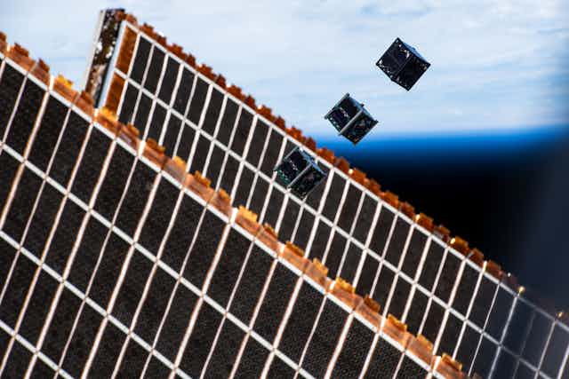 A small lack cube floating in space next to a grid of dark solar panels