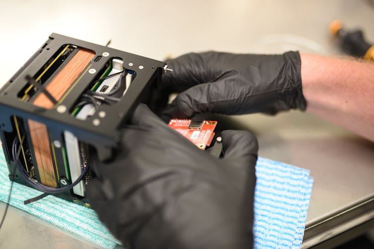 A pair of hands in dark gloves working on computing chips