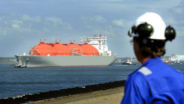A worker in blue overalls looks at a large vessel with red, bulbous tanks.