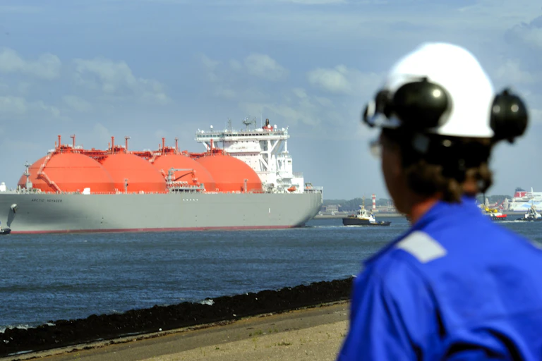 A worker in blue overalls looks at a large vessel with red, bulbous tanks.