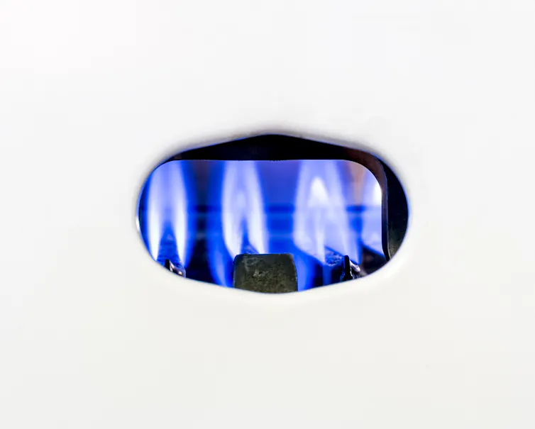 The blue pilot light inside a white gas boiler.