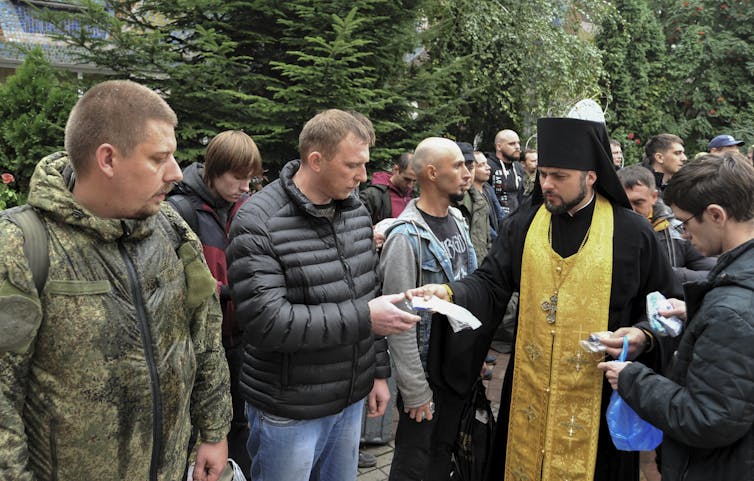 A Russian Orthodox priest walks through a crowd of men.