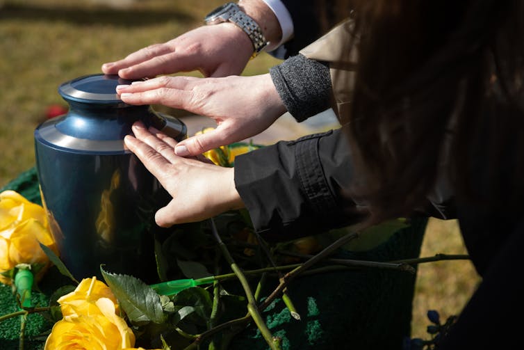 Plusieurs personnes tendent la main pour toucher l’urne funéraire d’un défunt