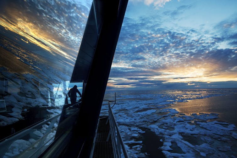 A man stands surveying the ice on an icebreaker as the sun lies low on the horizon.