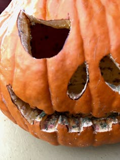 A freshly carved pumpkin with green dots in the mouth cuts