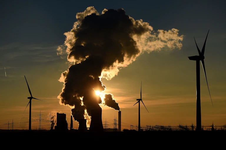 Power plants surrounded by wind turbines and electricity lines at sunset.