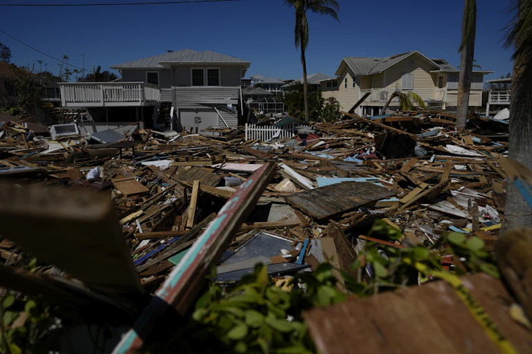wood and other wreckage from a home are scattered on the ground with less damaged houses in the distance
