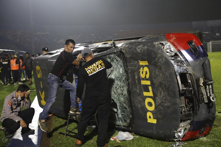 Officers examine a damaged police vehicle in a soccer stadium.