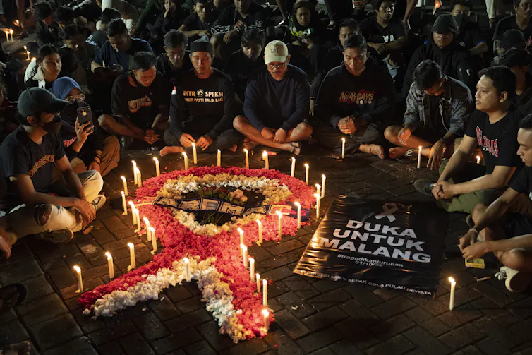 Personas sentadas alrededor de una vela encendida para conmemorar a las víctimas de la tragedia futbolística.