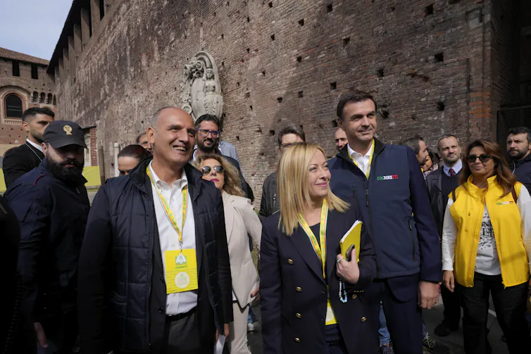 Giorgia Meloni en train de marcher dans une rue, entourée d’hommes et de femmes