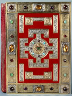 The red and bejewelled cover of a large book.