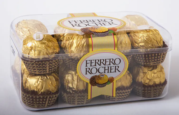 Transparent cuboid-shaped box of Ferrero Rocher chocolates, white background.