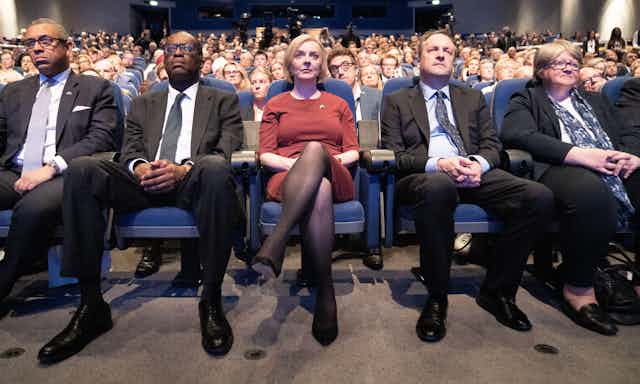 James Cleverly, Kwasi Kwarteng, Liz Truss, Hugh O'Leary and Thérèse Coffey sitting in a row in an audience, all looking glum.