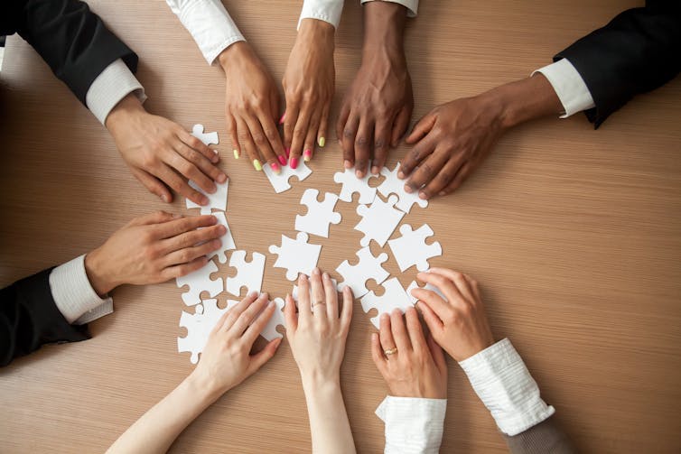Hands of a diverse group of people putting together a puzzle on a desk
