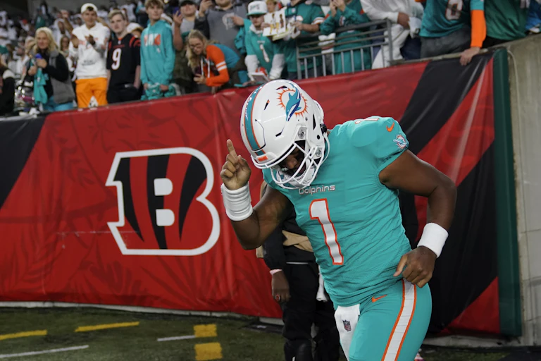 A man wearing a teal football uniform with the number 1 and a helmet jogging with his hand raised.
