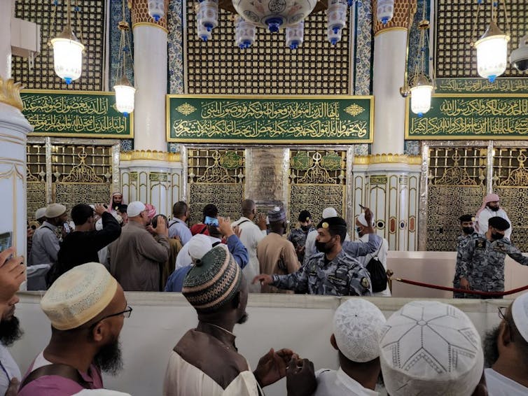 Men look at an ornately decorated shrine inside a mosque as security officers stand nearby.