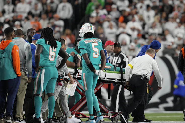 Officials with a stretcher are seen emerging from a cluster of men in teal football uniforms