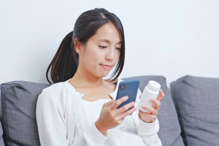 A person has their phone and holds a container of pills.