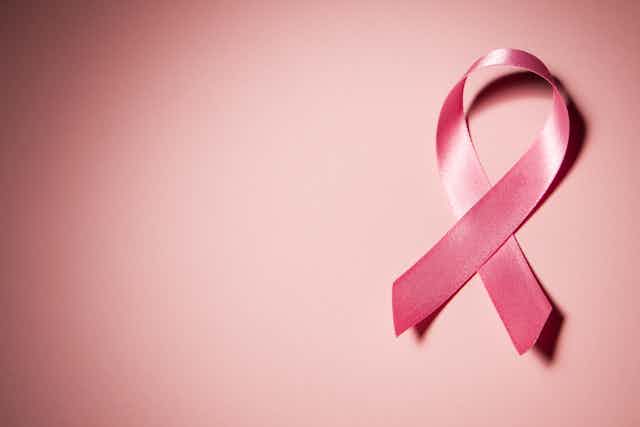 Pink breast cancer awareness ribbon on the right against a pink-hued background.
