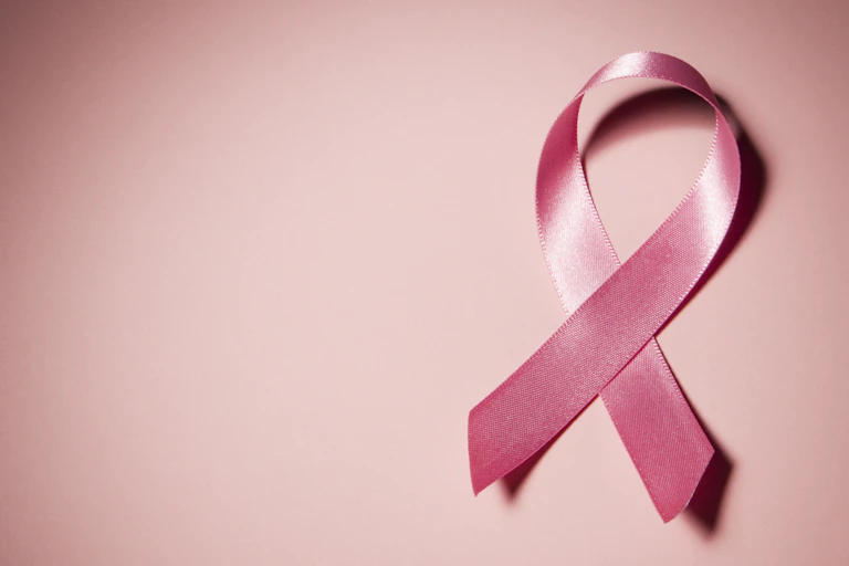 Pink breast cancer awareness ribbon on the right against a pink-hued background.