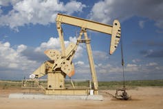 A close-up shot of a gas drilling unit in a rugged arid landscape against a cloudy blue sky.