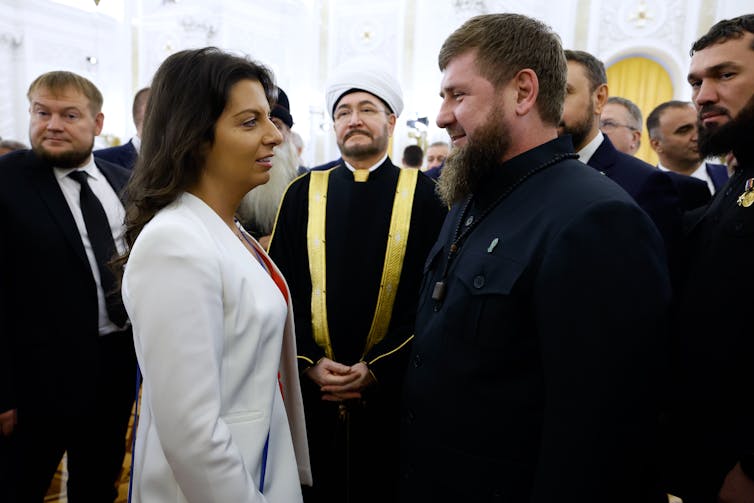 Хорошо одетые женщины и мужчины стояли лицом друг к другу в окружении толпы мужчин.