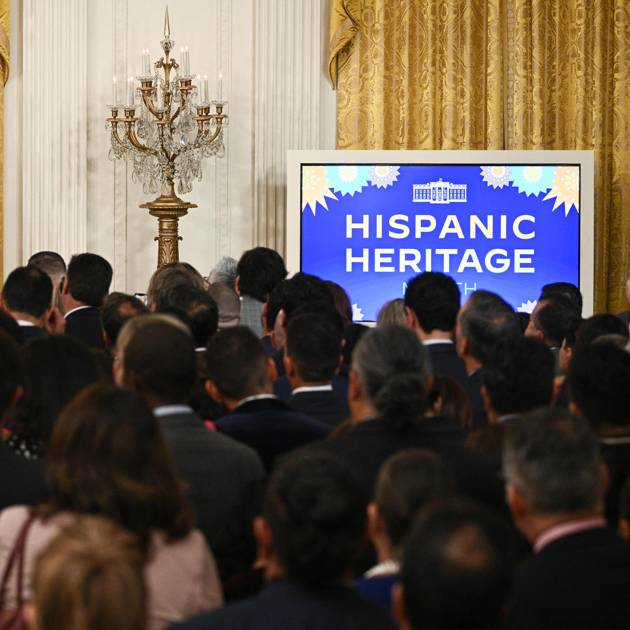 Biden at a lectern in front of a crowd, with a screen reading 'Hispanic Heritage'