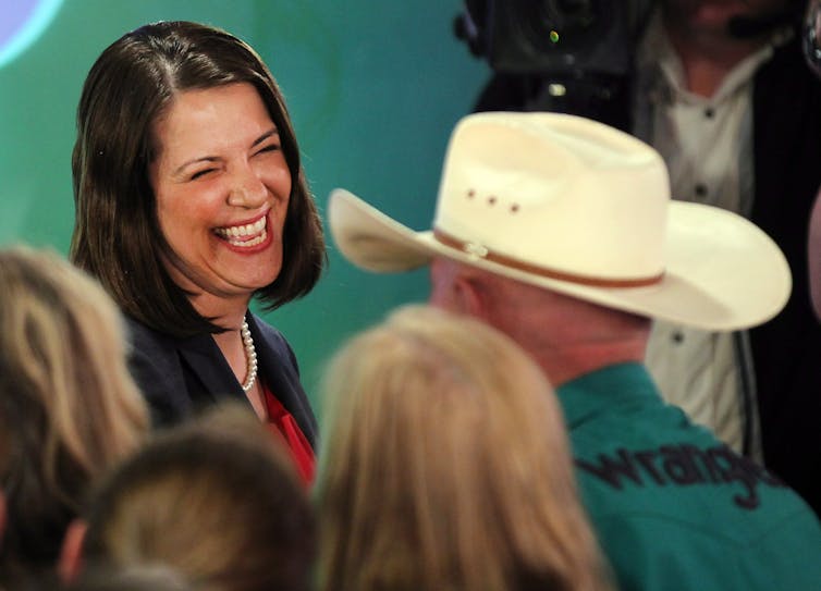 A woman smiles as she talks to a man in a cowboy hat.