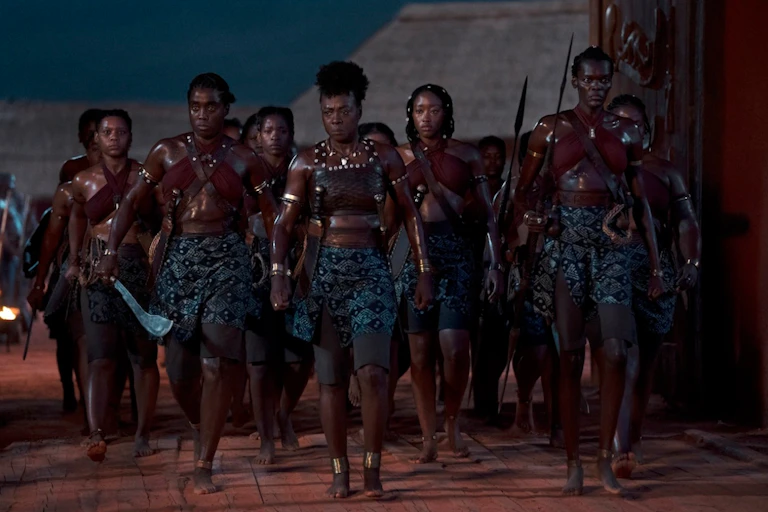A group of African women strides forward, dressed in military gear and carrying weapons.