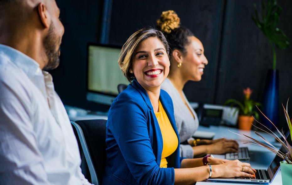 People seen facing a wall of computers with two people in discussion smiling.