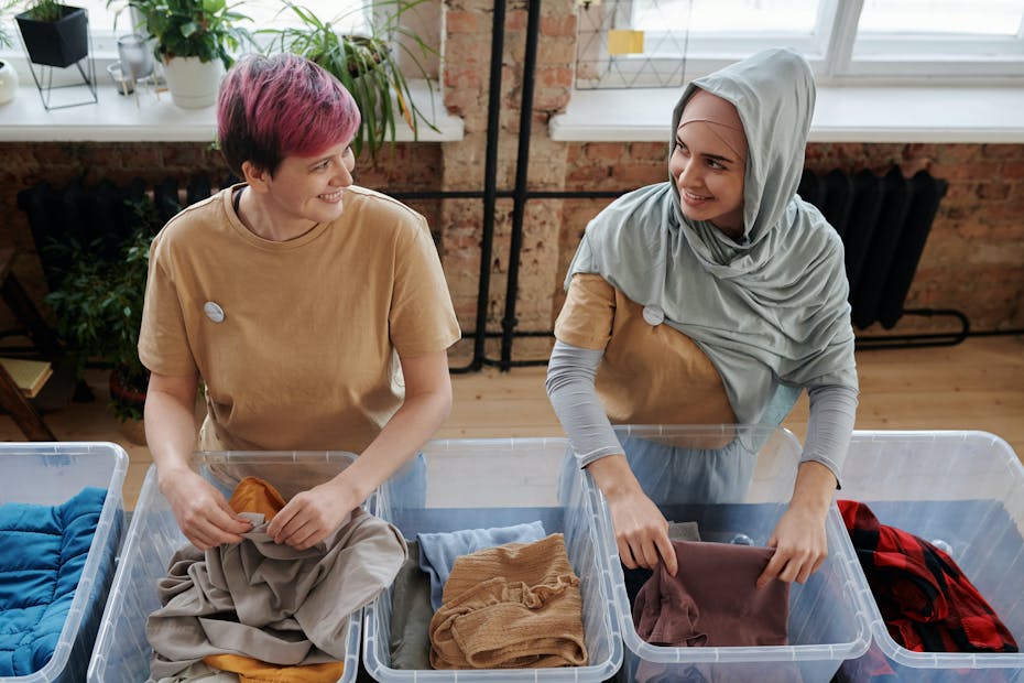 Two women seen sorting goods on a table smiling towards each other.