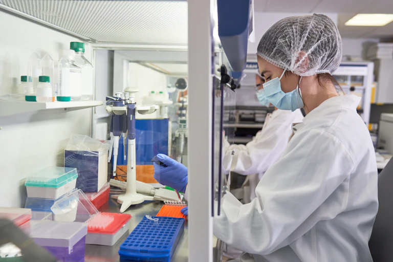 woman in protective gear pipetting under a hood