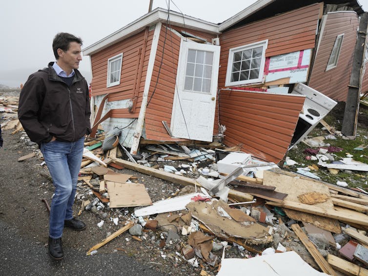 A dark-haired man looks at a destroyed house.