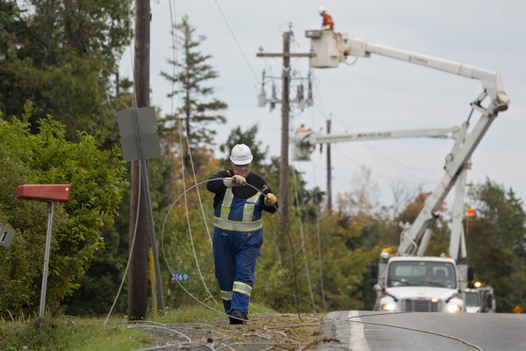 Power workers, one in a cherry-picker, repair downed power lines along a road.