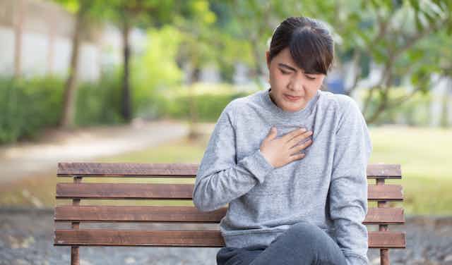 Woman sits on a bench holding her chest