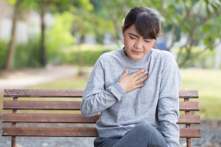Woman sits on a bench holding her chest